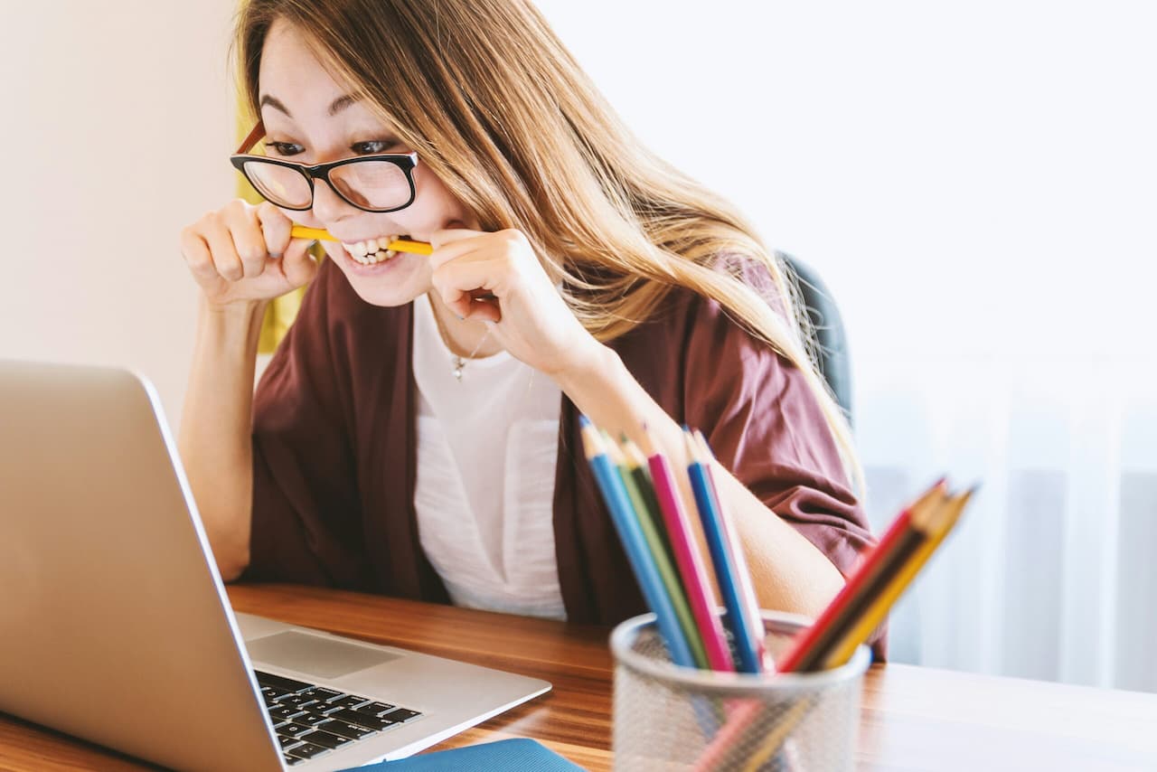 famale student sitting at computer desk biting pencil looking anxious